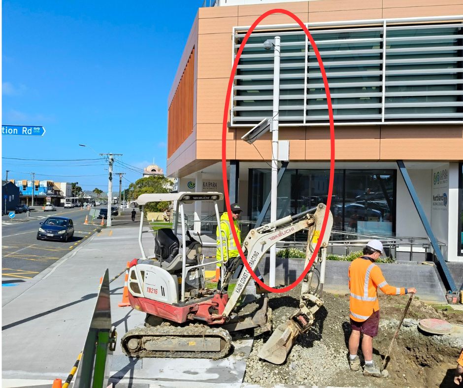 Street scene showing a road in foreground and building in background. At the pedestrian crossing a camera on a pole is installed. 